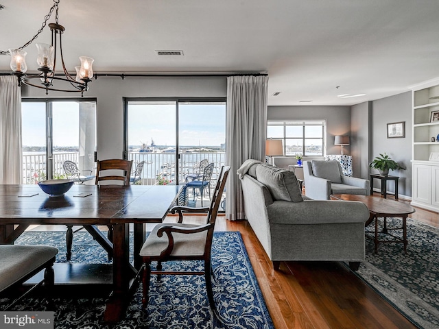 dining space featuring built in features, wood finished floors, visible vents, and a chandelier