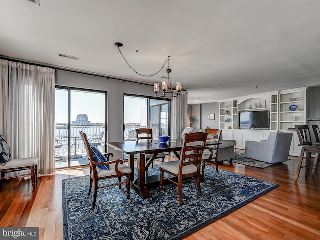 dining area featuring visible vents, built in shelves, an inviting chandelier, and wood finished floors