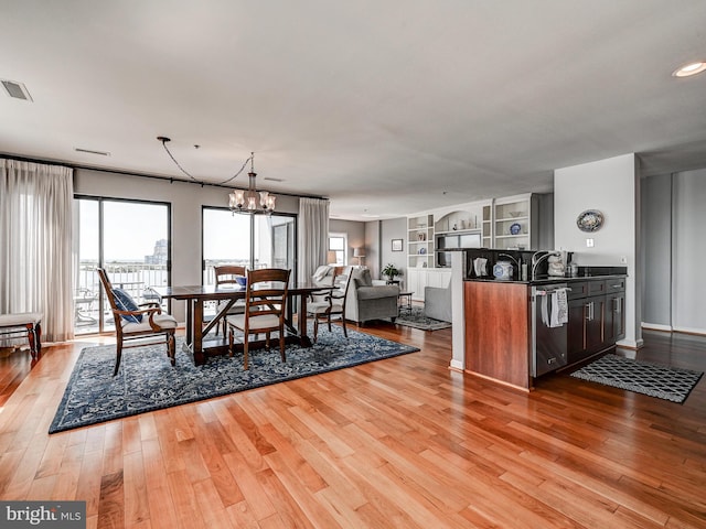 dining space with visible vents, built in features, an inviting chandelier, and wood finished floors