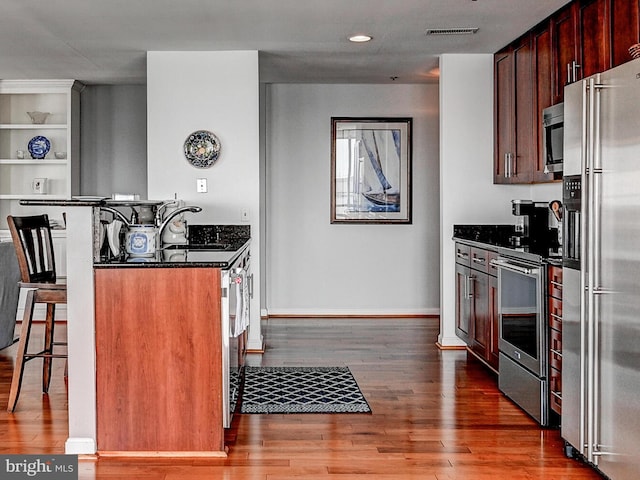 kitchen with wood finished floors, visible vents, baseboards, appliances with stainless steel finishes, and a kitchen bar