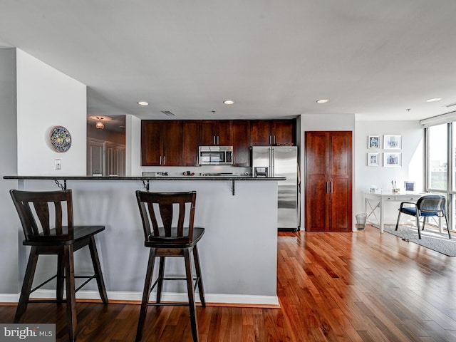 kitchen featuring hardwood / wood-style floors, recessed lighting, appliances with stainless steel finishes, a kitchen bar, and dark countertops