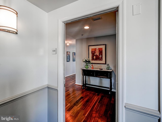 hall with dark wood finished floors, visible vents, and baseboards