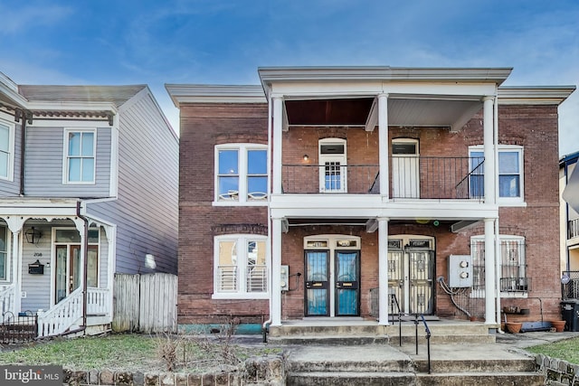 view of property featuring a balcony, fence, a porch, french doors, and brick siding