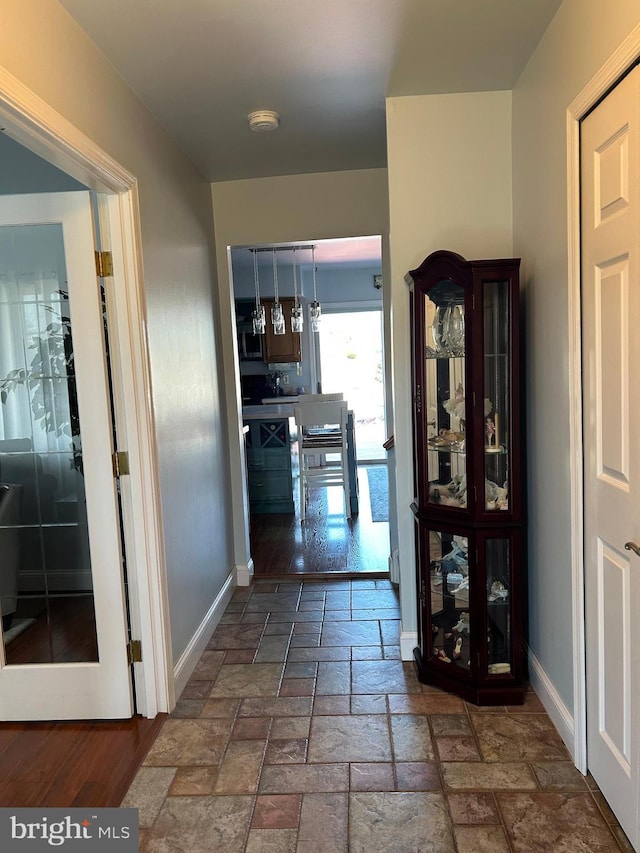 corridor with baseboards and stone tile floors