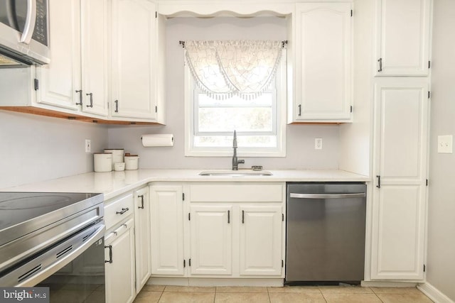 kitchen with light countertops, light tile patterned floors, appliances with stainless steel finishes, white cabinets, and a sink