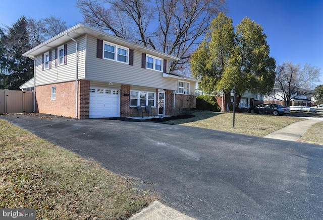 tri-level home featuring a front yard, fence, an attached garage, aphalt driveway, and brick siding