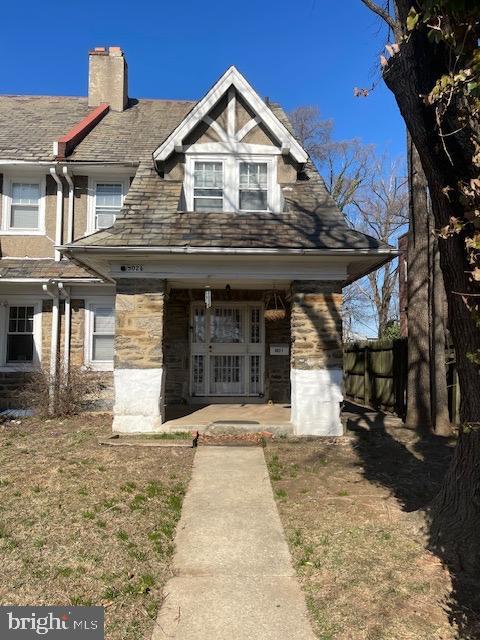 view of front of property featuring stone siding, a porch, a chimney, and fence