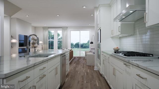 kitchen with a sink, white cabinetry, appliances with stainless steel finishes, wall chimney range hood, and light stone countertops