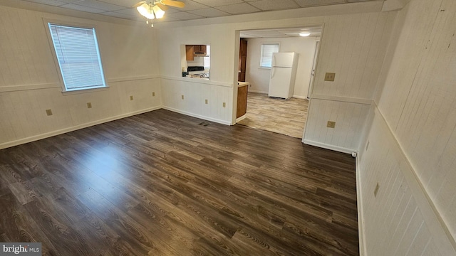 unfurnished room with a drop ceiling, a healthy amount of sunlight, ceiling fan, and dark wood-style flooring