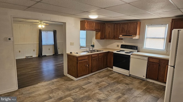 kitchen with under cabinet range hood, dark wood finished floors, light countertops, white appliances, and a sink