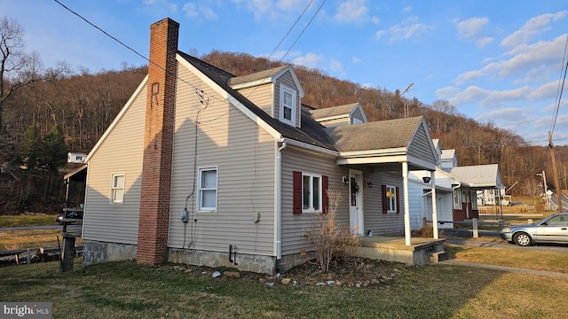 view of property exterior with a shingled roof, a yard, and a chimney