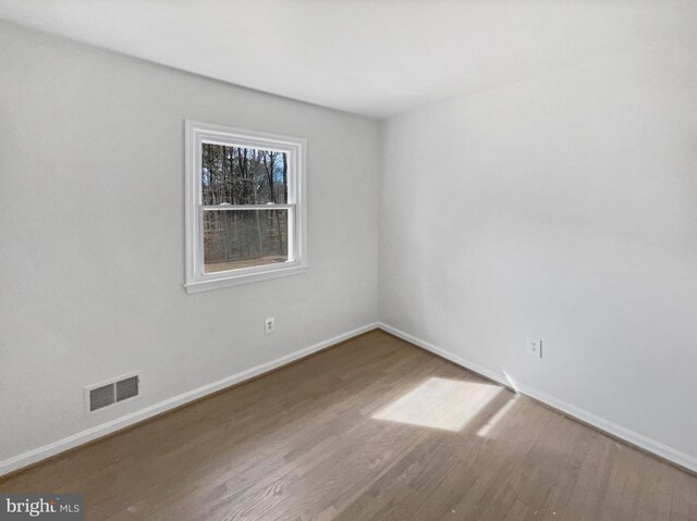 empty room featuring wood finished floors, visible vents, and baseboards