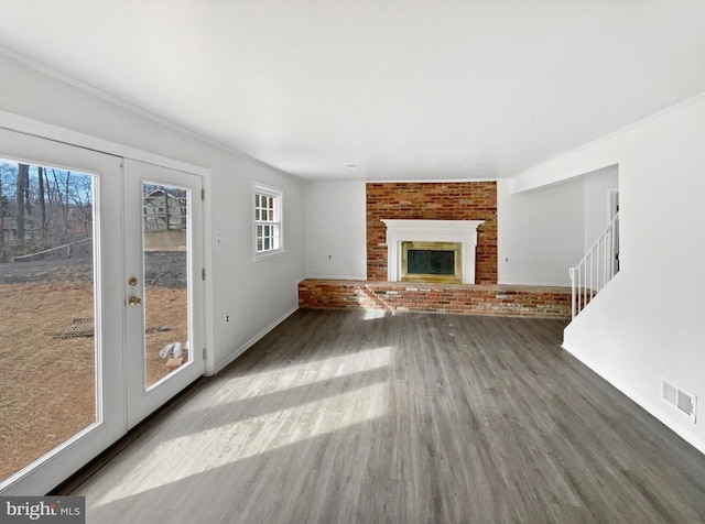 unfurnished living room featuring wood finished floors, visible vents, stairs, french doors, and a brick fireplace