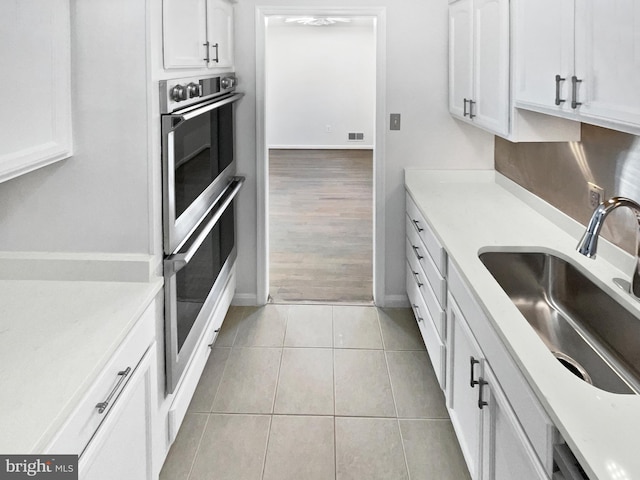 kitchen with white cabinetry, light tile patterned flooring, stainless steel double oven, and a sink