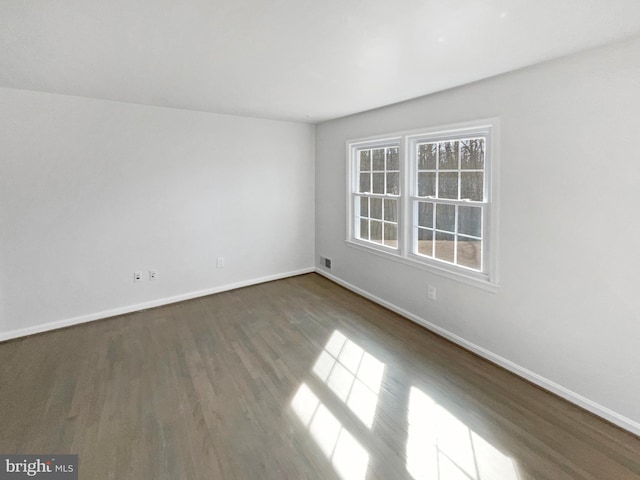 spare room with visible vents, baseboards, and dark wood-type flooring