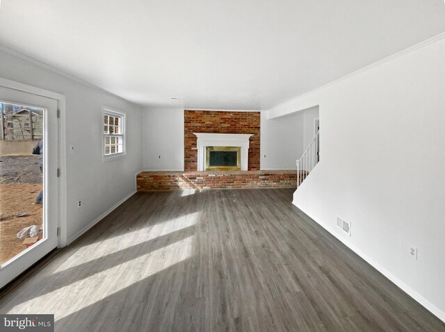 unfurnished living room with visible vents, a brick fireplace, brick wall, stairway, and wood finished floors