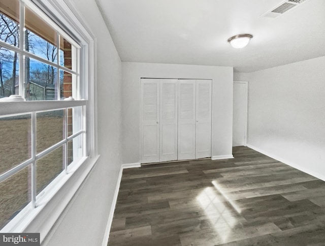 unfurnished bedroom featuring dark wood finished floors, visible vents, a closet, and baseboards