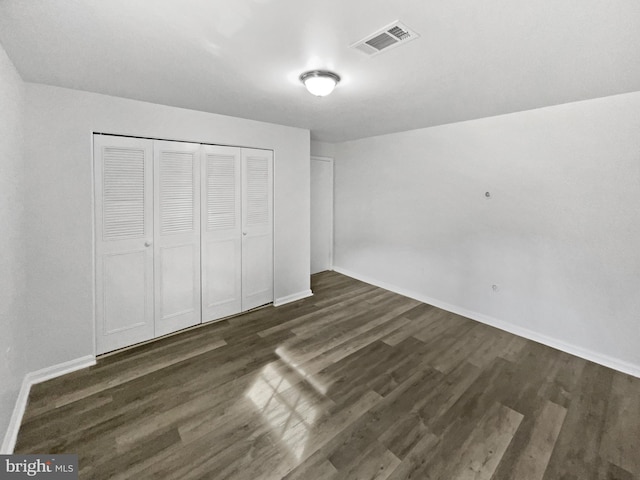 unfurnished bedroom with a closet, visible vents, baseboards, and dark wood-style flooring