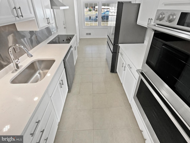 kitchen featuring light tile patterned floors, a sink, white cabinets, appliances with stainless steel finishes, and wall chimney exhaust hood