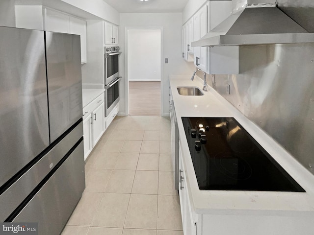 kitchen featuring light tile patterned floors, stainless steel appliances, a sink, white cabinetry, and wall chimney exhaust hood