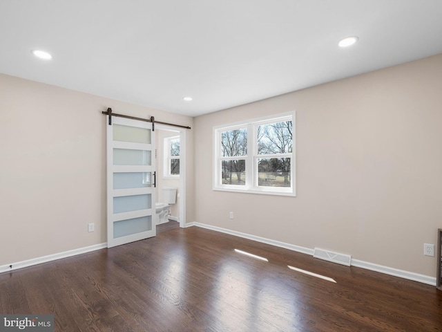 unfurnished bedroom with visible vents, baseboards, a barn door, recessed lighting, and wood finished floors