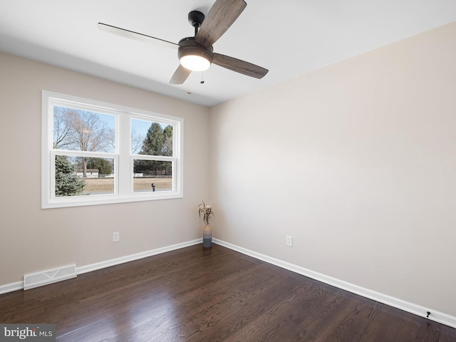 spare room featuring visible vents, a ceiling fan, dark wood-type flooring, and baseboards