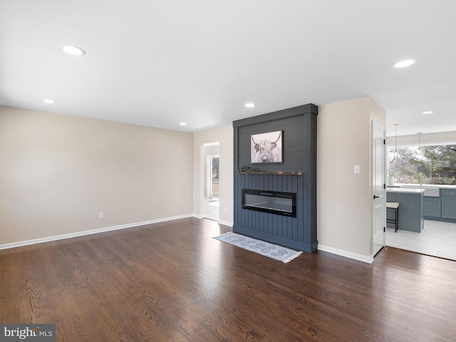 unfurnished living room featuring recessed lighting, wood finished floors, baseboards, and a large fireplace