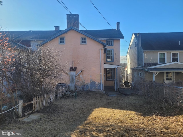 rear view of property featuring stucco siding, a chimney, and fence