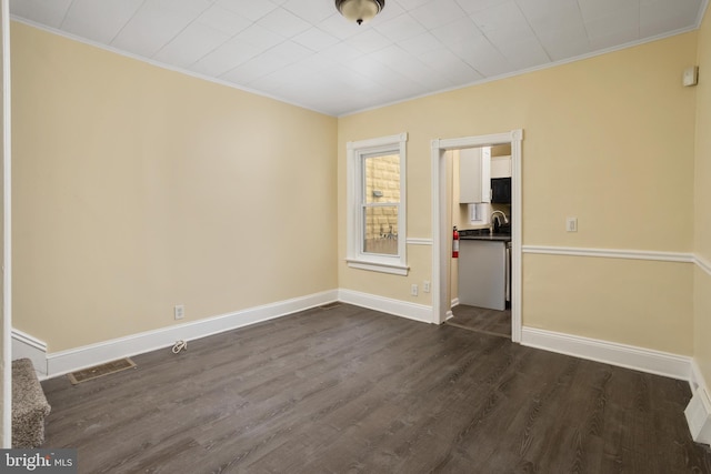 spare room featuring visible vents, a sink, dark wood finished floors, crown molding, and baseboards