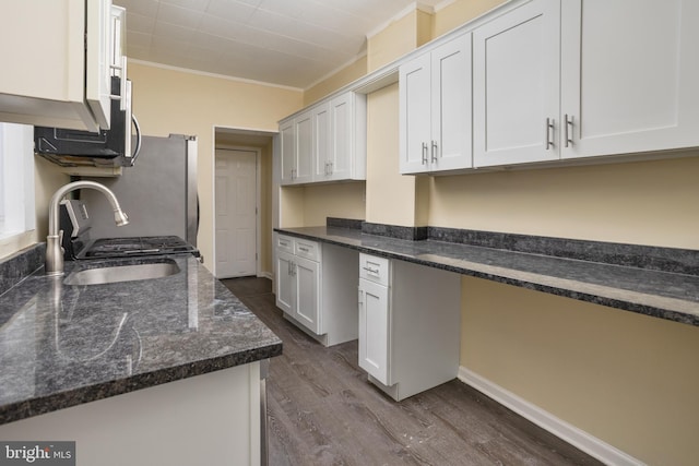 kitchen featuring dark wood-type flooring, ornamental molding, a sink, built in desk, and dark stone counters