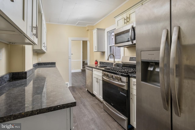 kitchen with a sink, dark stone counters, ornamental molding, appliances with stainless steel finishes, and dark wood-style flooring