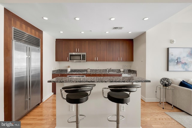 kitchen with stainless steel appliances, a kitchen bar, visible vents, and light wood-style flooring