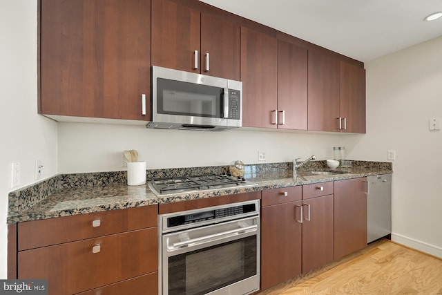 kitchen with dark stone countertops, light wood-type flooring, appliances with stainless steel finishes, and a sink