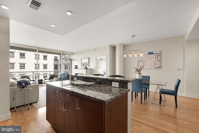 kitchen with dark stone countertops, visible vents, a kitchen island, pendant lighting, and light wood-type flooring