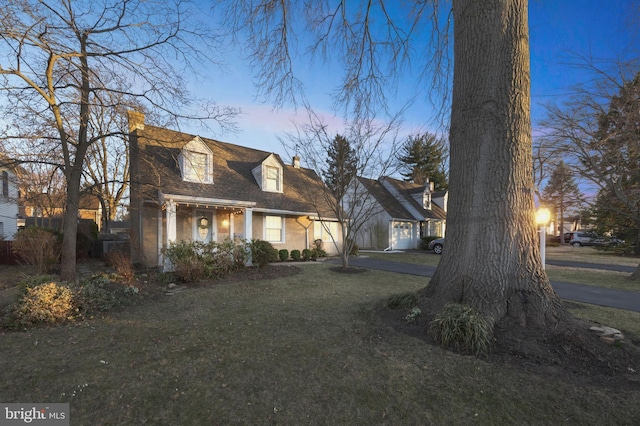 cape cod home with a shingled roof, a lawn, and a chimney