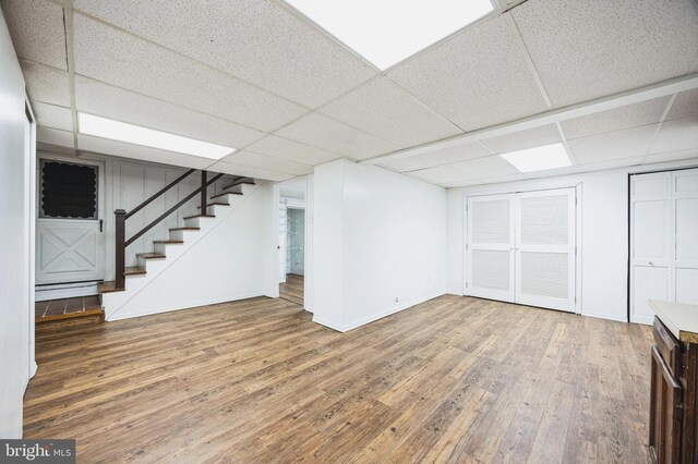 finished below grade area with a drop ceiling, stairway, baseboards, and wood finished floors