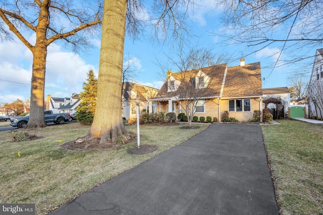 cape cod-style house featuring stucco siding, roof with shingles, a chimney, and a front lawn