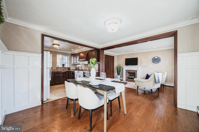 dining space featuring a baseboard radiator, ornamental molding, a brick fireplace, and wood finished floors