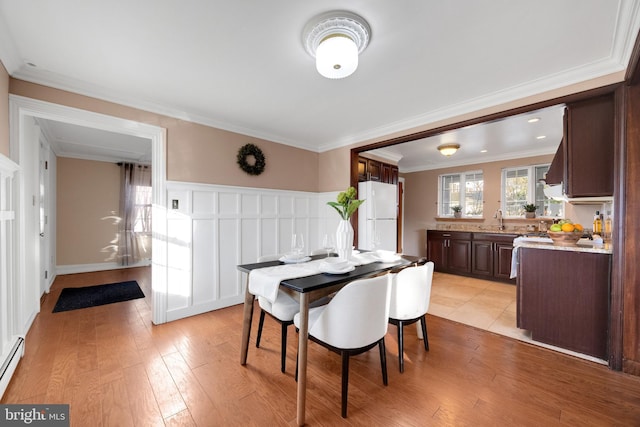 dining space featuring wainscoting, baseboard heating, light wood-style flooring, and crown molding