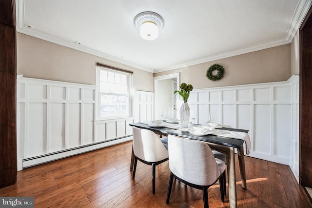 dining area with a wainscoted wall, a baseboard heating unit, wood finished floors, crown molding, and a decorative wall