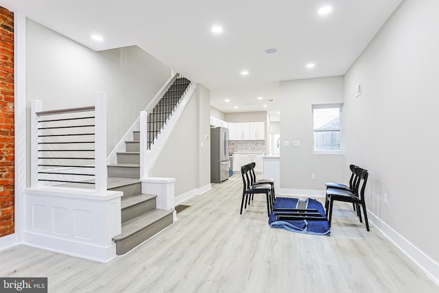 living area with stairway, baseboards, and light wood finished floors