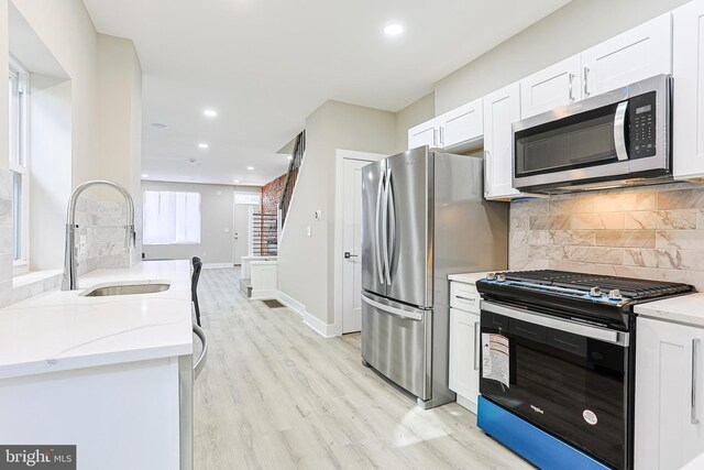kitchen featuring stainless steel appliances, decorative backsplash, a sink, light wood-style floors, and light stone countertops