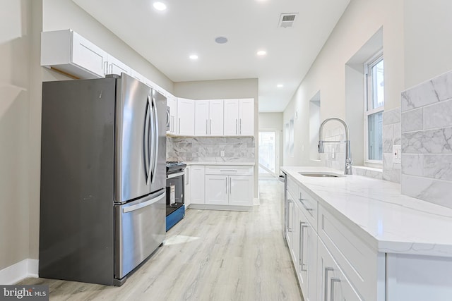 kitchen with a sink, light wood finished floors, light stone countertops, appliances with stainless steel finishes, and visible vents
