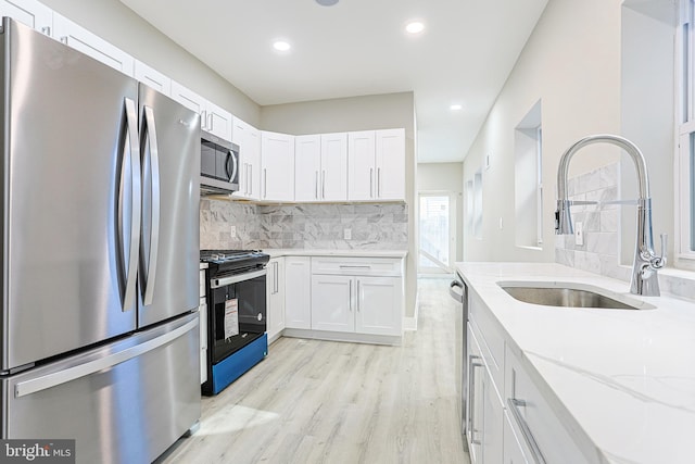 kitchen featuring light stone counters, a sink, appliances with stainless steel finishes, light wood-style flooring, and decorative backsplash