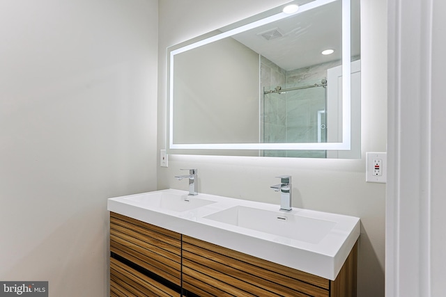 bathroom featuring double vanity, visible vents, a tile shower, and a sink
