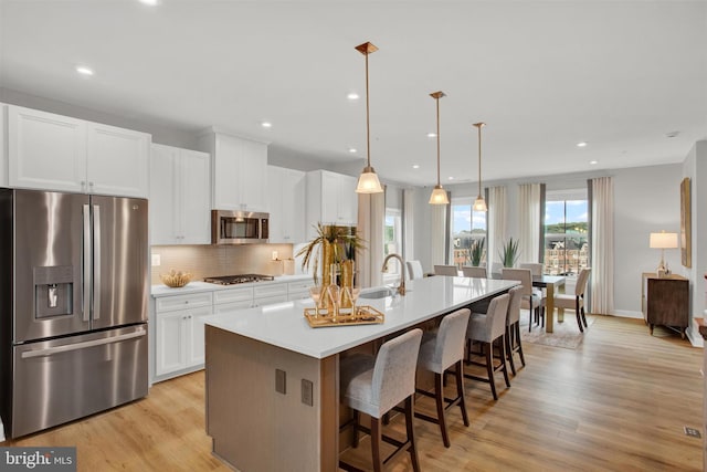 kitchen featuring light wood-style flooring, tasteful backsplash, a center island with sink, and stainless steel appliances