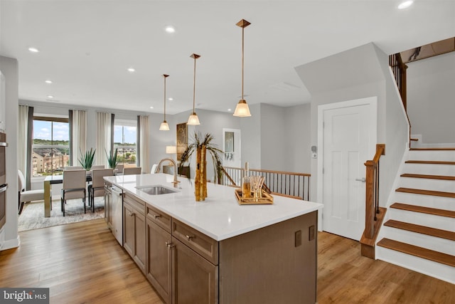 kitchen featuring a sink, dishwasher, light countertops, light wood-style floors, and a kitchen island with sink