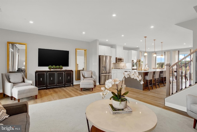 living room with recessed lighting, light wood-style flooring, stairs, and baseboards