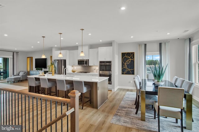 kitchen with a kitchen island with sink, white cabinetry, light wood-style floors, appliances with stainless steel finishes, and light countertops