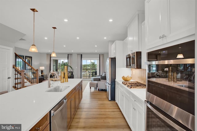 kitchen with light wood-style flooring, a sink, light countertops, appliances with stainless steel finishes, and open floor plan